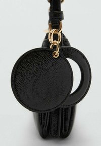 Borsa in finta pelle nera con dettagli in metallo dorato, dotata di un'etichetta tonda con superficie testurizzata e un dettaglio a ritaglio circolare.