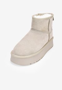 Stivale alla caviglia in suede beige con fodera morbida, punta rotonda e suola piatta spessa. Presenta un risvolto e dettagli cuciti.