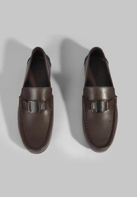 Bruine leren loafers met een gladde afwerking, voorzien van een zilverkleurige metalen gesp en stiksel langs de randen. Ontwerp met platte zool.