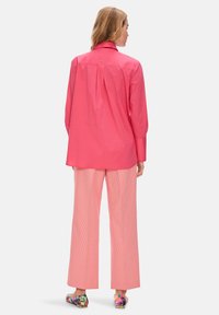 Light pink button-up shirt with a back pleat, paired with striped pale pink wide-leg pants and floral-accented loafers.