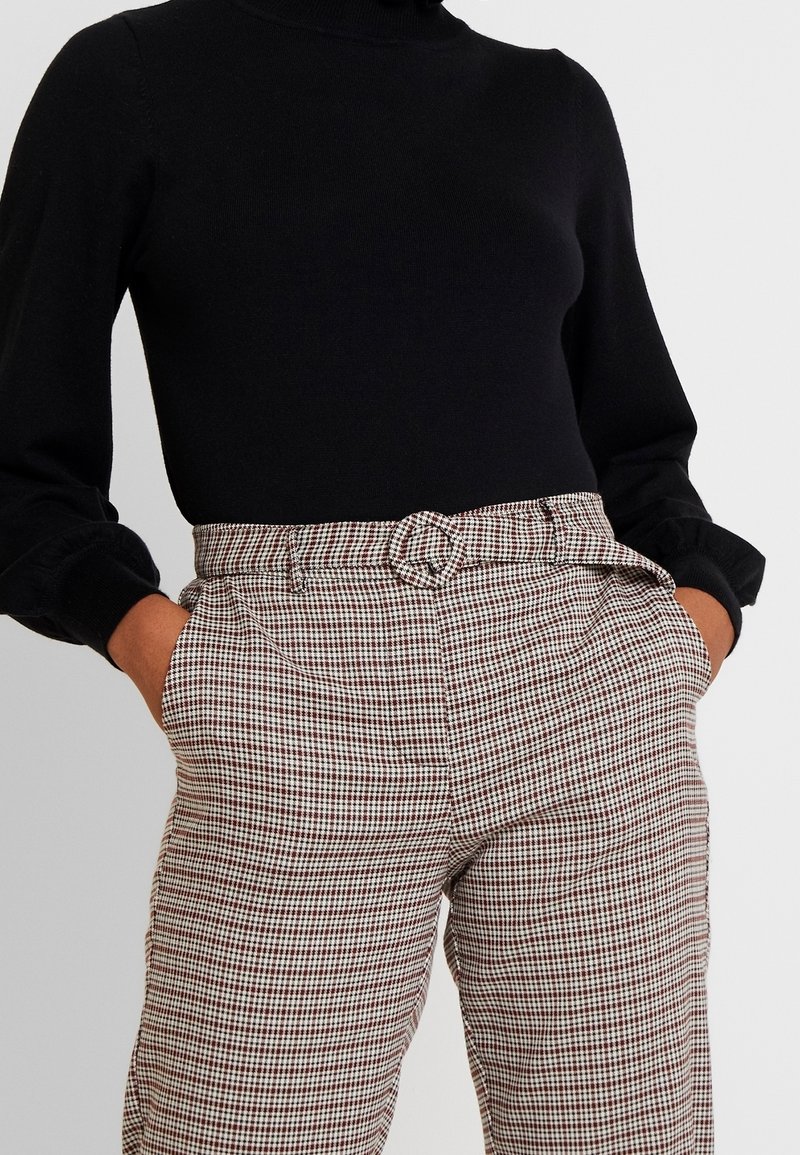 Černý rolák spárovaný s hnědými a bílými kostkovanými kalhotami s vysokým pasem, které mají detail vázaného opasku a boční kapsy.
