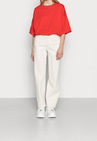 T-shirt rossa oversize con maniche corte, abbinata a pantaloni bianchi a gamba dritta e sneakers bianche. Design semplice, vestibilità casual.