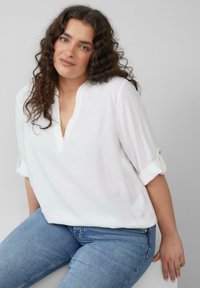 Witte linnen blouse met een V-hals en opgerolde mouwen. Gecombineerd met blauwe denim jeans, met een casual, relaxed pasvorm.