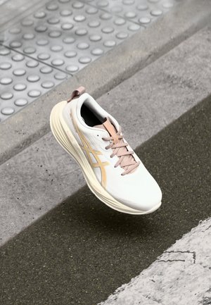 Hardloopschoen in wit met beige accenten, met een gladde textuur, ronde vorm en een gevoerde kraag. Veters zijn lichtroze.