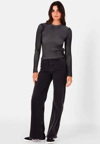 Zwarte geribbelde top met lange mouwen en verticale strepen, gecombineerd met zwarte flared jeans en zwarte sneakers. Soepele textuur, casual pasvorm.