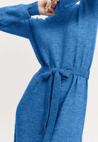 Robe en tricot bleu à manches longues, décolleté montant et ceinture assortie nouée à la taille. Texture douce et silhouette décontractée.