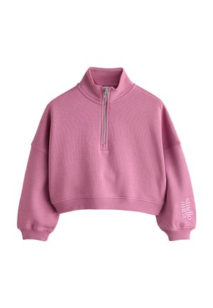 Lyserød cropped sweatshirt med halv lynlås og høj krave samt lange ærmer, med teksten "studio amrta" på venstre manchet.