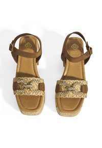 Braune Wildledersandalen mit einer Korksohle, ausgestattet mit einem dekorativen, geflochtenen Riemen mit einem metallischen Akzent. Verstellbarer Knöchelriemen für den perfekten Sitz.