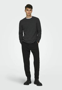 Donkergrijze longsleeve shirt met een witte ronde hals, gecombineerd met zwarte broek en zwarte laarzen; eenvoudig ontwerp met een relaxed pasvorm.