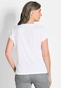 Witte t-shirt met korte mouwen en opgerolde mouwen, met een ronde hals, gemaakt van lichtgewicht stof, gezien van achteren tegen een neutrale achtergrond.