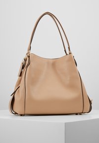 Sac à main en cuir beige avec une forme décontractée, deux poignées pour les épaules, une surface texturée et des accents en métal doré.