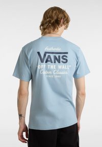 Svetle modré bavlněné tričko s kulatým výstřihem, které na přední straně má velké tmavě modré logo "VANS" a na zadní straně bílé písmo, a krátké rukávy.