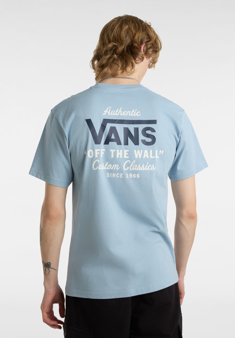 Svetle modré bavlněné tričko s kulatým výstřihem, které na přední straně má velké tmavě modré logo "VANS" a na zadní straně bílé písmo, a krátké rukávy.