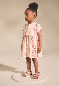 Világos rózsaszín ruha virágos és tündér mintával, rövid, felsliccelt ujjal és gyűrt derékkal. Barna szandál dupla pánttal és texturált talppal.