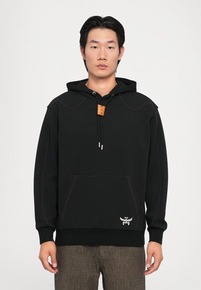 Sudadera con capucha negra hecha de tejido suave, con costuras naranjas, un cordón de cuero con ajuste y un bolsillo canguro en la parte frontal.