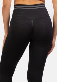 Zwarte leggings met een geribde hoge tailleband met grijze strepen. Soepele textuur, aansluitende pasvorm, minimale zichtbare stikseldetails.