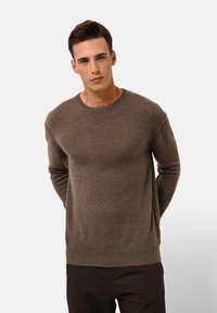 Brauner Pullover aus einem weichen, strukturierten Material. Hat einen runden Ausschnitt, lange Ärmel und ein dezentes Steppdetail an der Schulter.