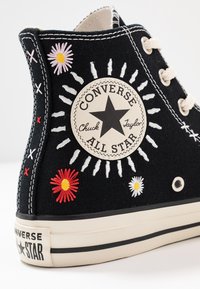 Černé plátěné tenisky vysokého střihu s vyšívanými květinami, ikonickou nášivkou loga, krémovými tkaničkami a gumovou podrážkou s černým pruhem.