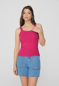 Aansluitend roze tanktop van ribbed stof, met brede schouderbanden en een ronde halslijn, gecombineerd met lichtblauwe denim shorts met voorzakken.