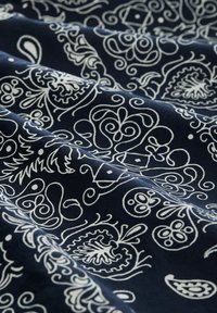 Marineblauer Stoff mit weißen, filigranen Floral- und Paisleymustern, dargestellt mit sanften Falten, die Licht- und Schattenkontraste erzeugen.