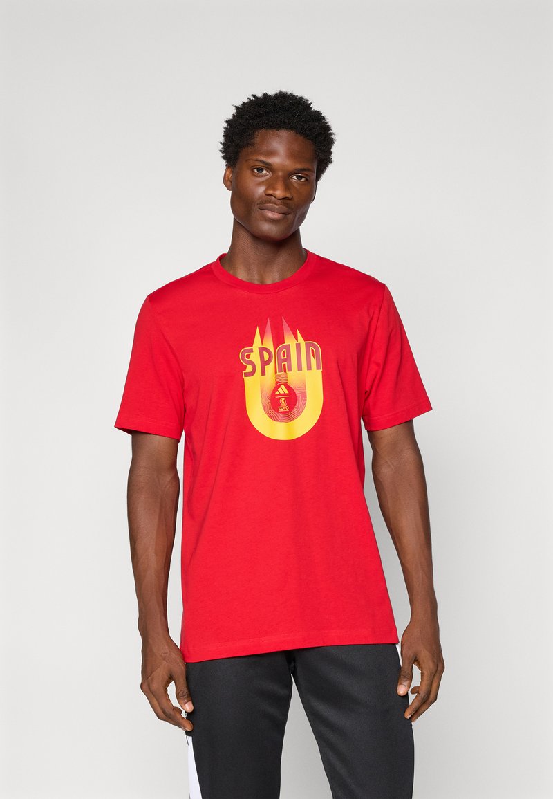 Rød bomulds t-shirt med et gult og rødt grafisk design samt teksten "SPAIN" og flamme-lignende detaljer centreret på brystet.