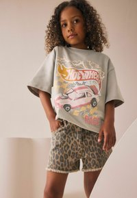 Harmaa ylisuuria t-paita, jossa on "Hot Wheels" -grafiikka; farkkushortsit leopardikuosisella ja repaleisella helmalla; malli poseeraa kädet taskuissa.
