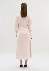 Rochie lungă cu mâneci lungi, de culoare roz deschis, cu un corset ajustat și o fustă evazată, având mâneci îngrijite și un material neted, ușor lucios.