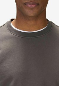 Mörkgrå sweatshirt i bomull med rund halsringning och platta sömmar. Har en kontrasterande vit inre krage som detalj.