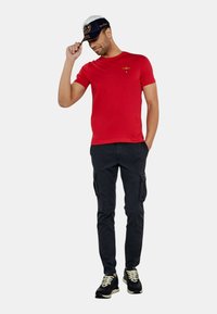 T-shirt rossa a maniche corte con un piccolo design ricamato sul petto, abbinata a pantaloni cargo neri e sneakers nere.