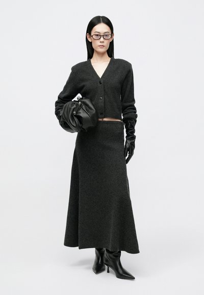 Γυναίκα με σκούρο γκρίζο πουκάμισο με κουμπιά, μακρύ συνδυασμένο φούστα, μαύρες δερμάτινες γάντια, μπότες, κρατώντας μια μαύρη δερμάτινη τσάντα clutch και γυαλιά.