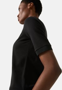 Czarny krótki rękaw z dopasowanym krojem, wykonany z teksturowanej tkaniny z subtelnym logo wytłoczonym z boku.