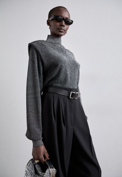 Pantalones negros de cintura alta con pliegues, combinados con una blusa de manga larga texturizada en gris. Los accesorios incluyen un bolso reflectante y gafas de sol oscuras.