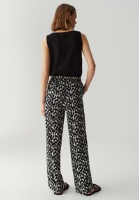 Zwart gebreid mouwloos topje, loszittende gebloemde broek met een zwart en crème geometrisch ontwerp, gedragen met platte sandalen.