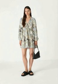 Λουλουδάτο μίνι φόρεμα με μακριά φουσκωτά μανίκια, που διαθέτει λεπτομέρεια με κορδόνι στον λαιμό. Συνδυάζεται με μια μαύρη τσάντα χειρός και σανδάλια.