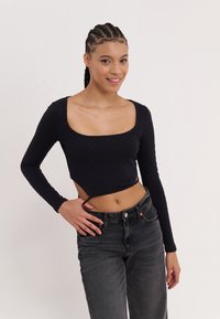 Black long-sleeve top with a square neckline and a cropped design, featuring textured fabric. Paired with high-waisted dark jeans.