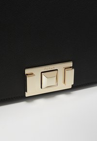 Borsa nera in pelle con una chiusura in hardware dorato, dettagli geometrici e una superficie texturizzata. Logo del marchio impresso sulla chiusura.