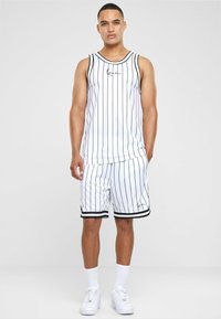 Hvid tanktop og shorts sæt med lodrette sorte striber, der har en sort kant og et lille logo på brystet og shortsene.