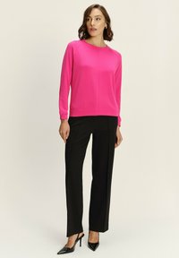 Felpa fucsia con maniche raglan, abbinata a pantaloni neri su misura e tacchi a punta neri. Tessuto morbido, design minimalista.