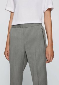 Pantalons à rayures grises avec une texture lisse, dotés de poches zippées sur les côtés et d'une taille plate. Associés à un t-shirt blanc uni.