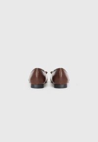 Ballerines en cuir marron au design simple, à bout rond et talon bas noir. Présentent un petit nœud décoratif.