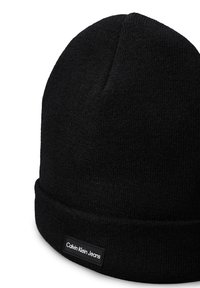 Fekete kötött sapka hajtott mandzsettával, amelyen egy téglalap alakú címke látható, rajta "Calvin Klein Jeans" felirattal, fehér színben. Simább textúra és egyszerű dizájn.