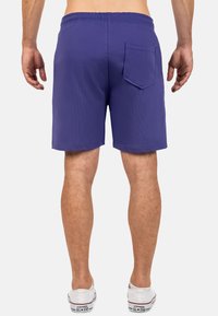 Pantaloni corti viola con vita elasticizzata e una sola tasca posteriore. Realizzati in tessuto morbido, con una texture liscia e un design fino al ginocchio.