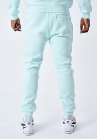 Pantalones de chándal verde menta claro con puños elásticos, un bolsillo trasero y una textura suave, combinados con zapatillas deportivas Nike blancas con acentos negros.