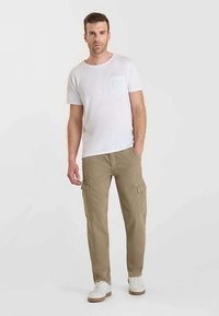 Camiseta blanca de cuello redondo con un bolsillo en el pecho, combinada con pantalones cargo color caqui claro que tienen bolsillos laterales, usada con zapatillas blancas.