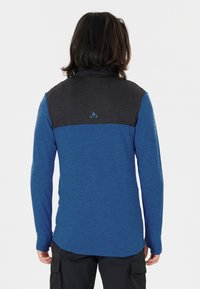 Långärmad skjorta med blå kropp, svart texturerad axelparti och en logotyp på baksidan. Materialet verkar mjukt och lätt.