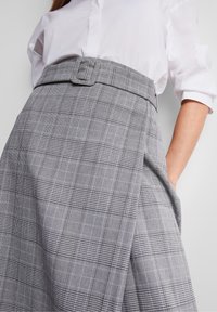 Gonna a quadri grigia con una cintura larga e dettagli in cintura, caratterizzata da più motivi e un tessuto testurizzato, abbinata a una camicia bianca.