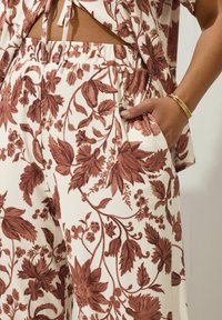 Blommönstrade vida byxor i grädde med rostfärgade botaniska mönster. Har elastisk midja och sidofickor. Strukturerad tyg.