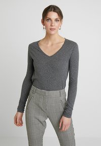 Pilka ilgomis rankovėmis V formos iškirpte, pagaminta iš minkštos medžiagos, derinama su aukštu juosmeniu juodai baltos langelių rašto kelnėmis.