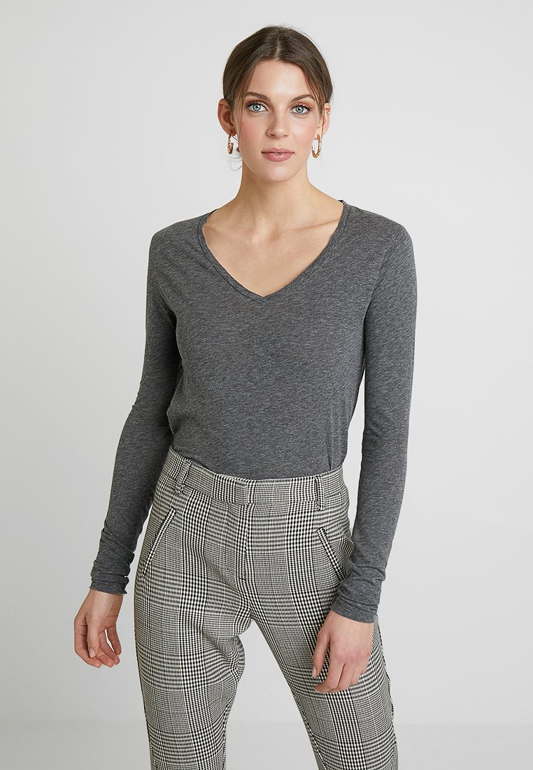 Pilka ilgomis rankovėmis V formos iškirpte, pagaminta iš minkštos medžiagos, derinama su aukštu juosmeniu juodai baltos langelių rašto kelnėmis.