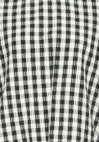 Tissu vichy noir et blanc avec un petit motif à carreaux et une couture visible passant verticalement par le centre.